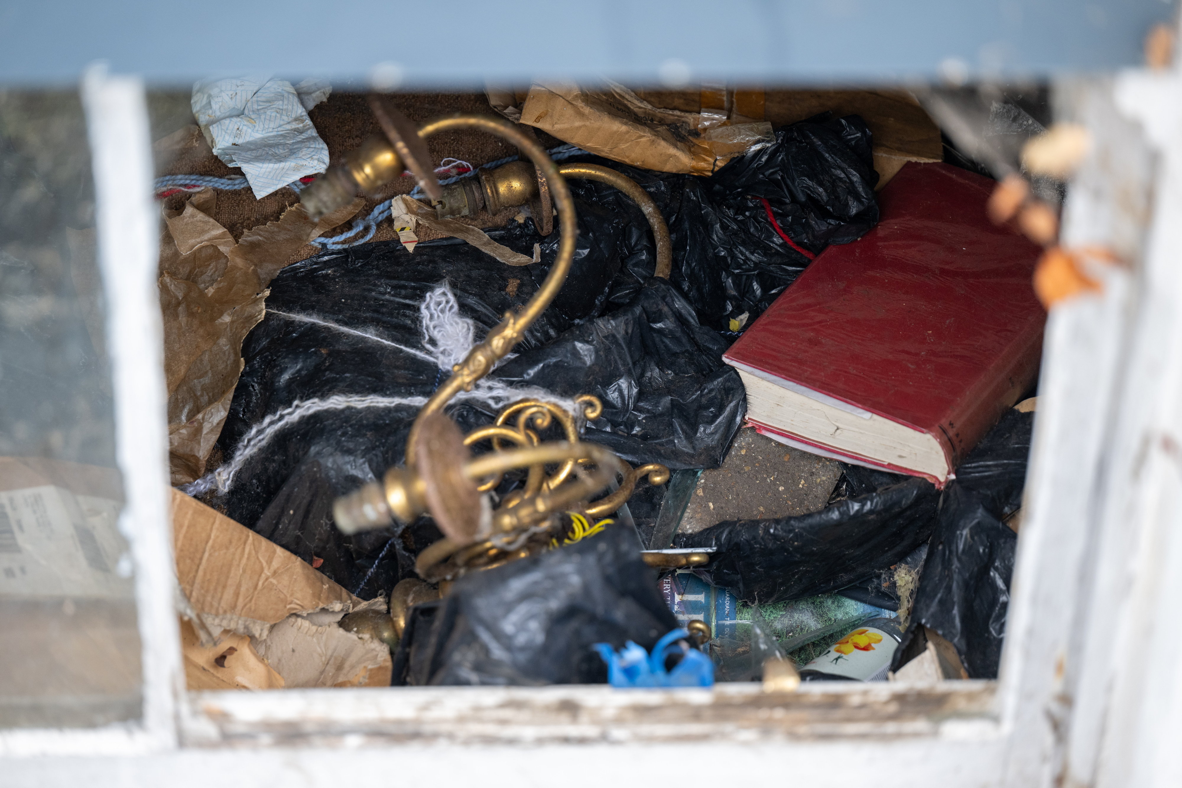 A cluttered view through a window of trash bags, an old book, and other debris.