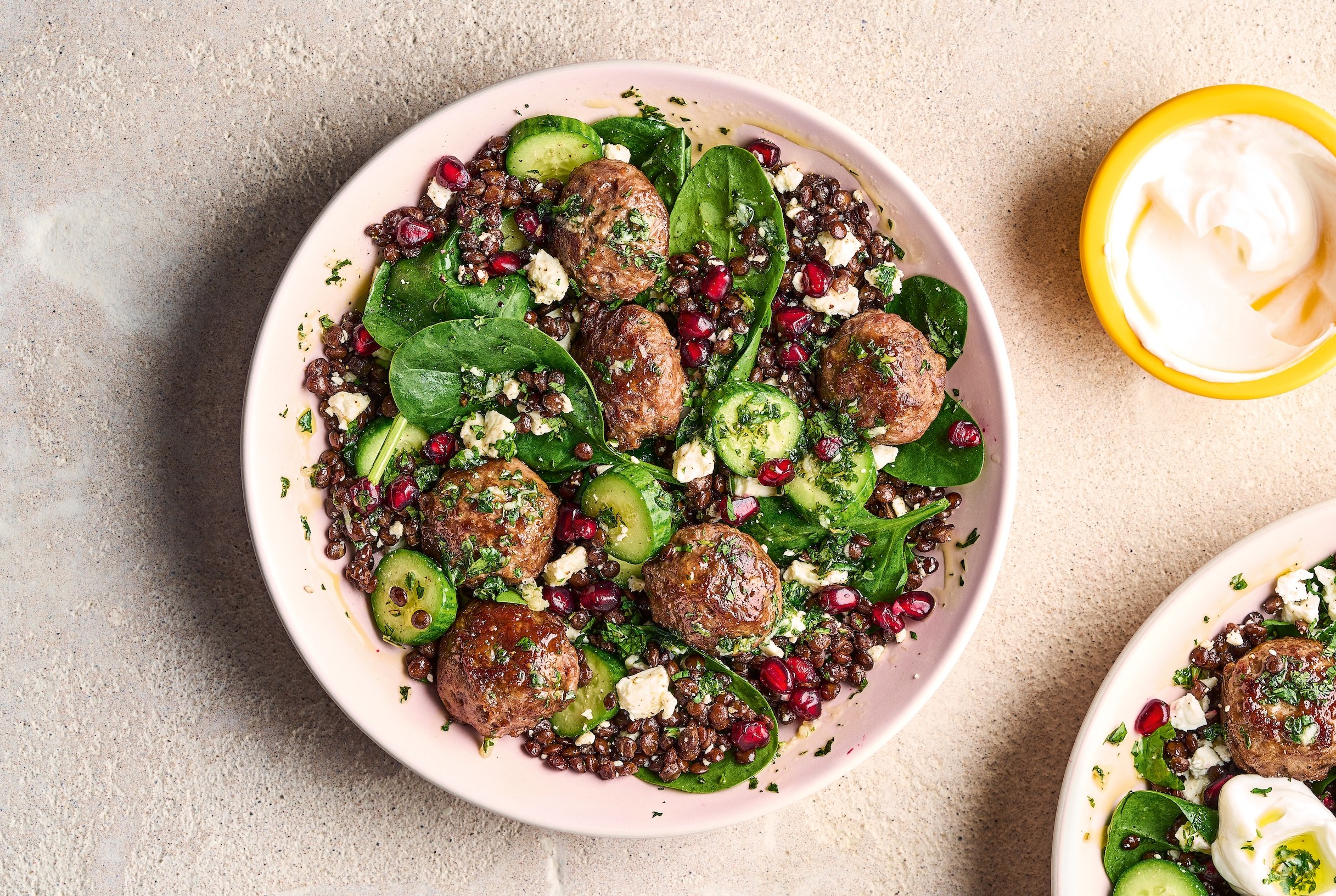 Meatball and lentil salad with spinach, pomegranate seeds, and cucumber, served with a side of yogurt.