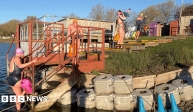 Young 18 year old man sits in the passenger seat of a black VW car, his arm resting on the open window as he looks to camera