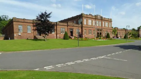 Philip Halling A large sandstone building with grass lawns and trees in front of it and a road