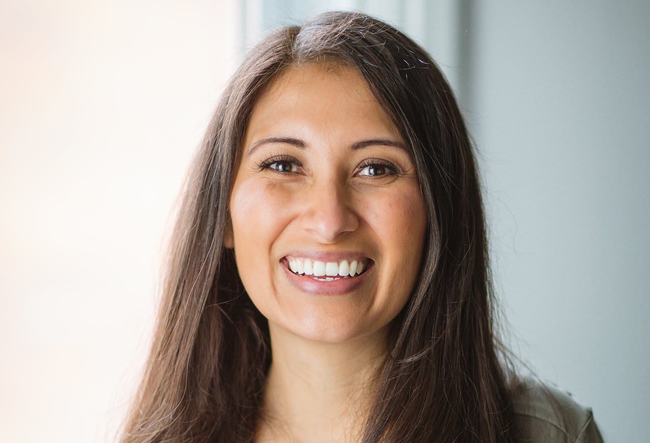 Woman with long dark chair smiles wearing olive green top