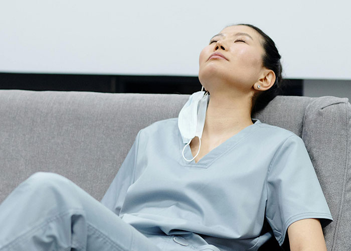 Psychiatric institution worker in scrubs resting on a sofa after a stressful and unforgettable work shift.