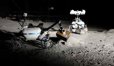 Two white rovers lean over simulated gray lunar dust.