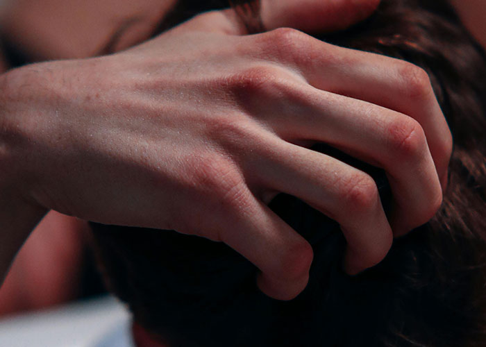 Close-up of a hand gripping a person's head, illustrating stress experienced by psychiatric institution workers on the job.