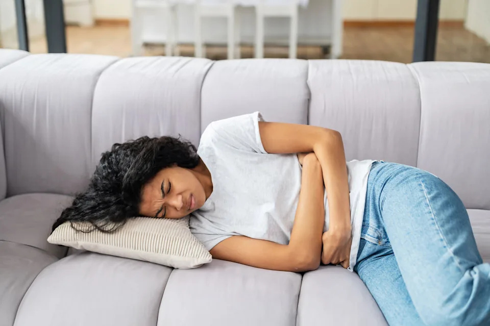 Young woman lying on a sofa and suffering from a stomach ache