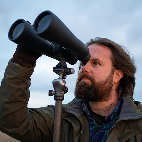 Author holding large Celestron binoculars gazing at the sky