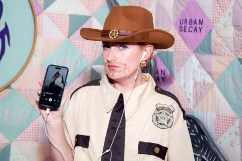 Getty Images  Amelia Dimoldenberg shows how she's listening to a Lily Allen song while dressed as a sheriff