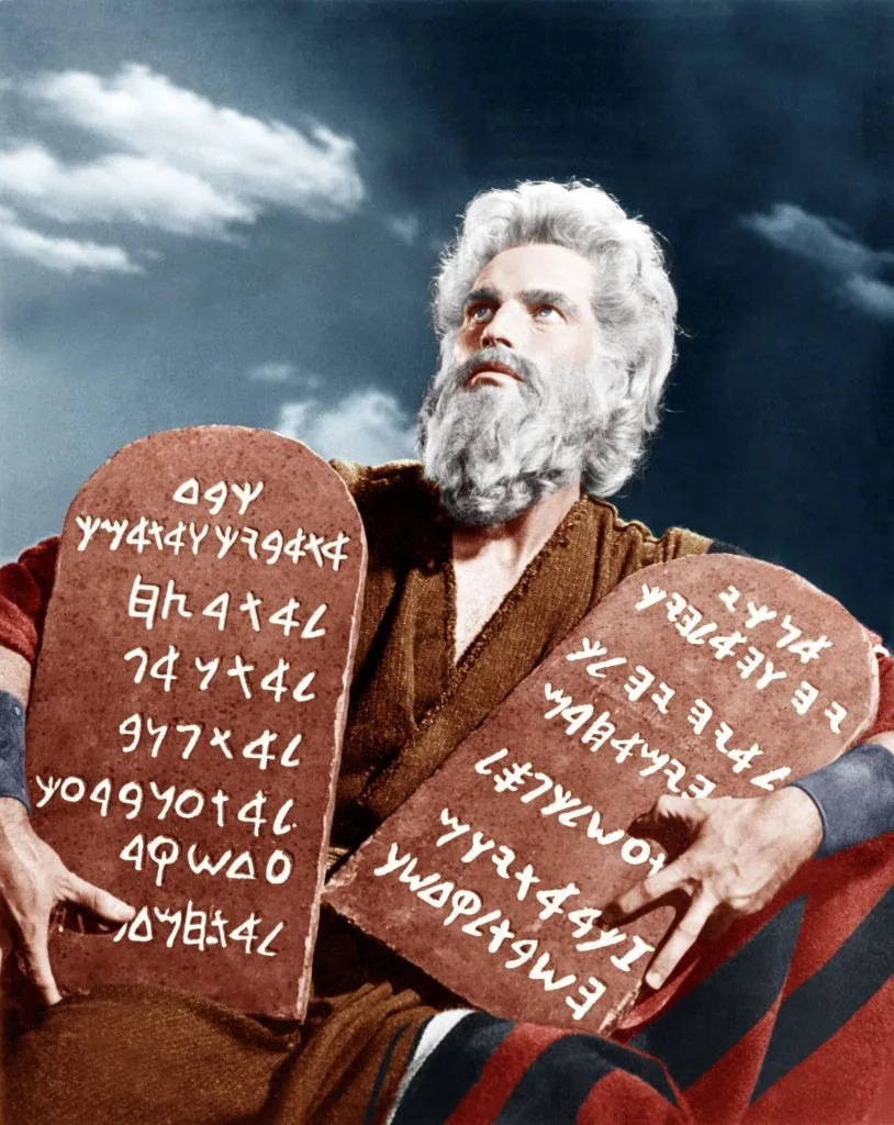 Charlton Heston as Moses, holding two stone tablets with ancient script, evoking a biblical scene