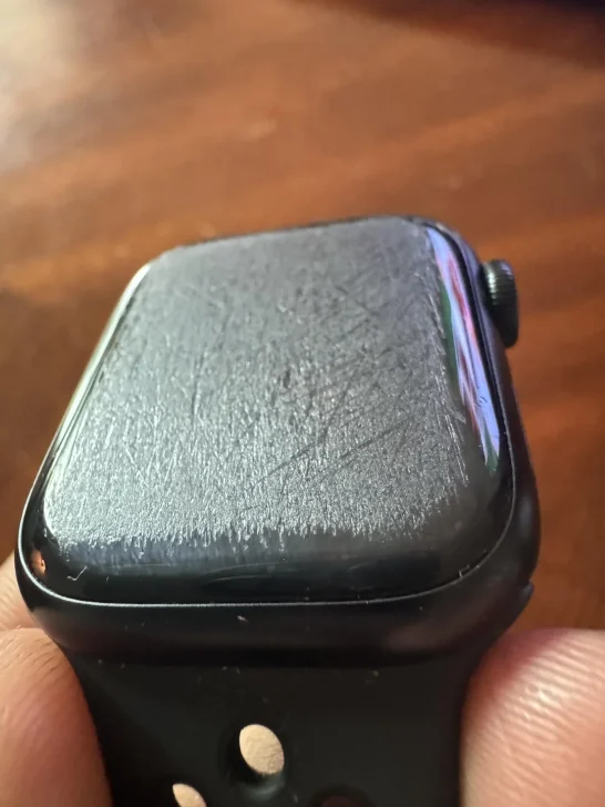 A heavily scratched screen on an Apple Watch with a black band.