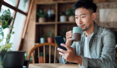 Young Asian man drinking coffee at home and looking at his phone