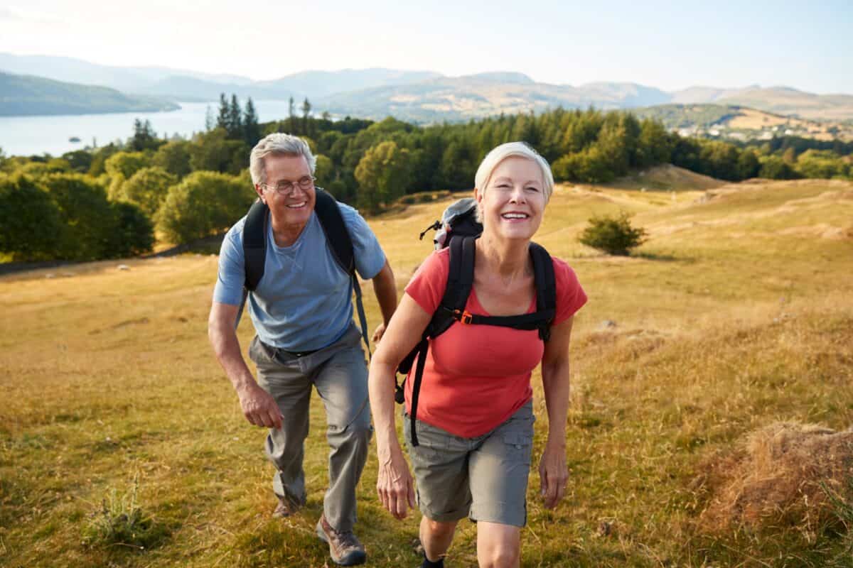Portrait Of Senior Couple Climbing Hill On Hike Through Countryside In Lake District UK Together