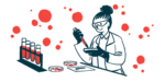 A scientist works with a petri dish in a lab, in front of a rack holding four vials filled with liquid.
