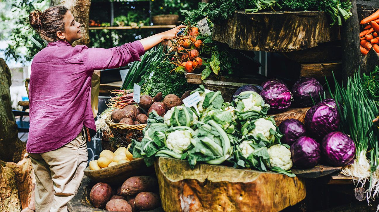 young woman in fuchsia shirt picking vegetables at the market