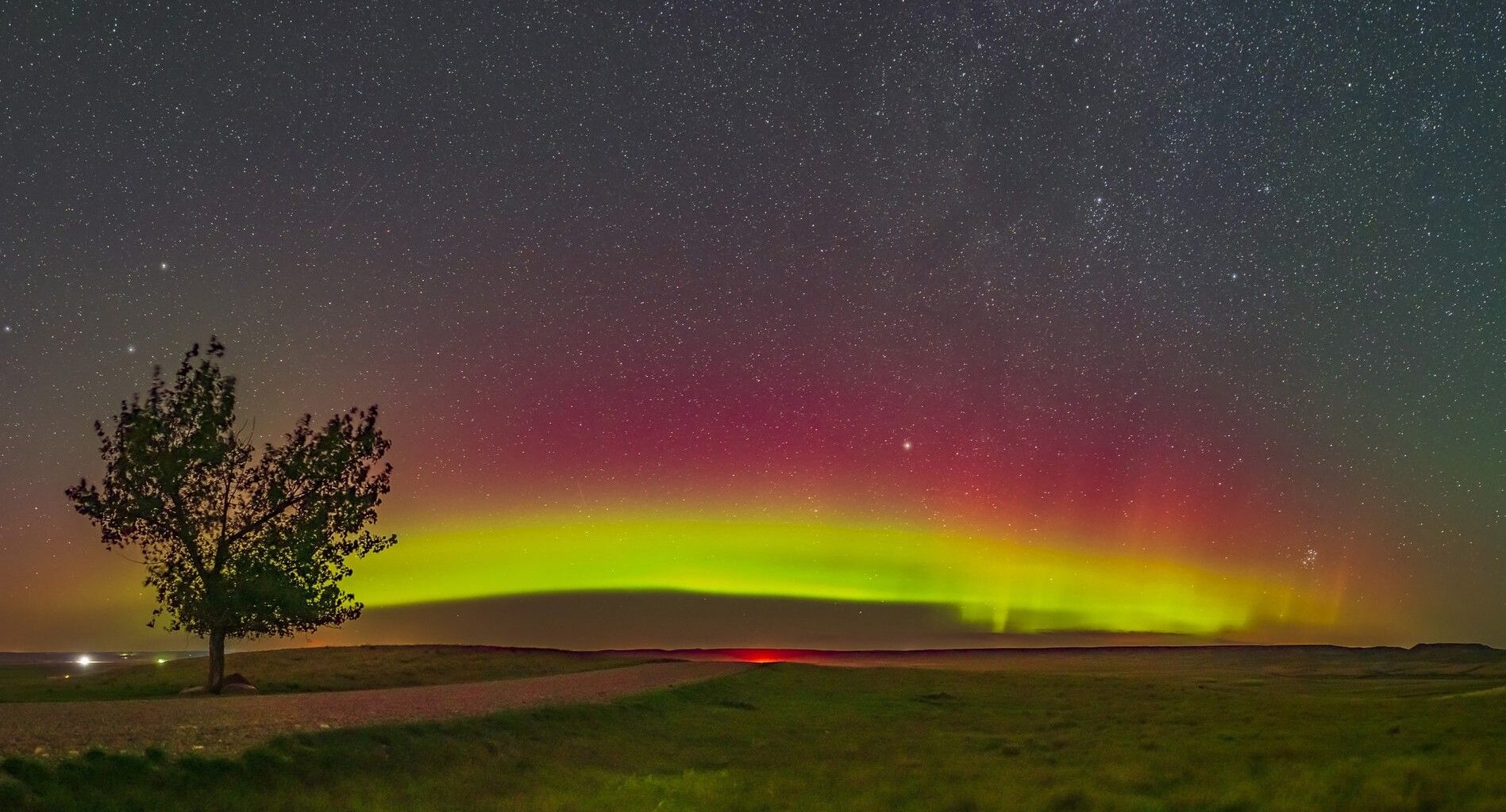 aurora arc above farmland, the sky glows magenta and green.
