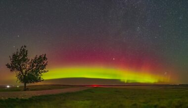 aurora arc above farmland, the sky glows magenta and green.