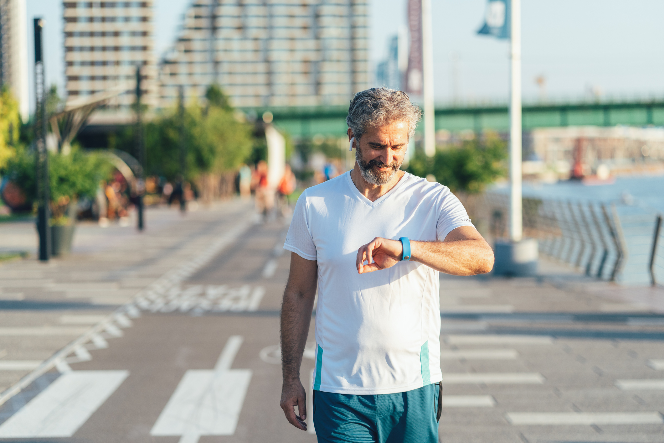 Man walking in city next to body of water looking at a blue sports watch