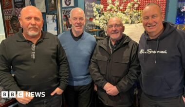 Four men in a line all wearing dark colours. These are left to right