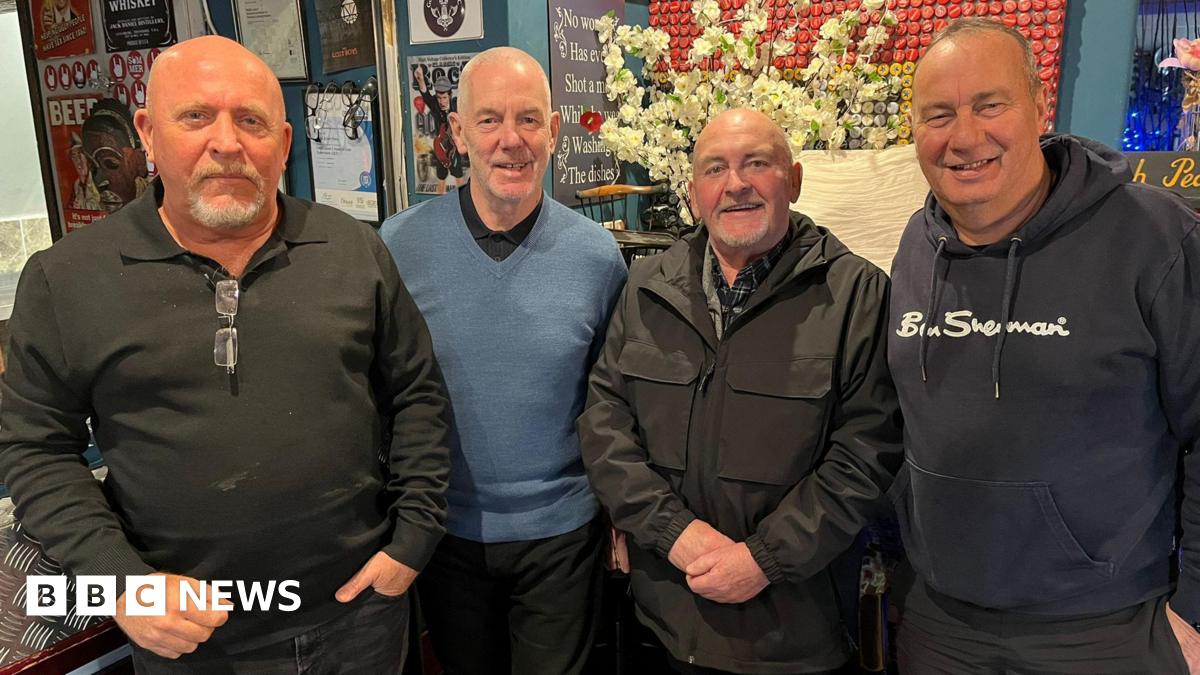 Four men in a line all wearing dark colours. These are left to right