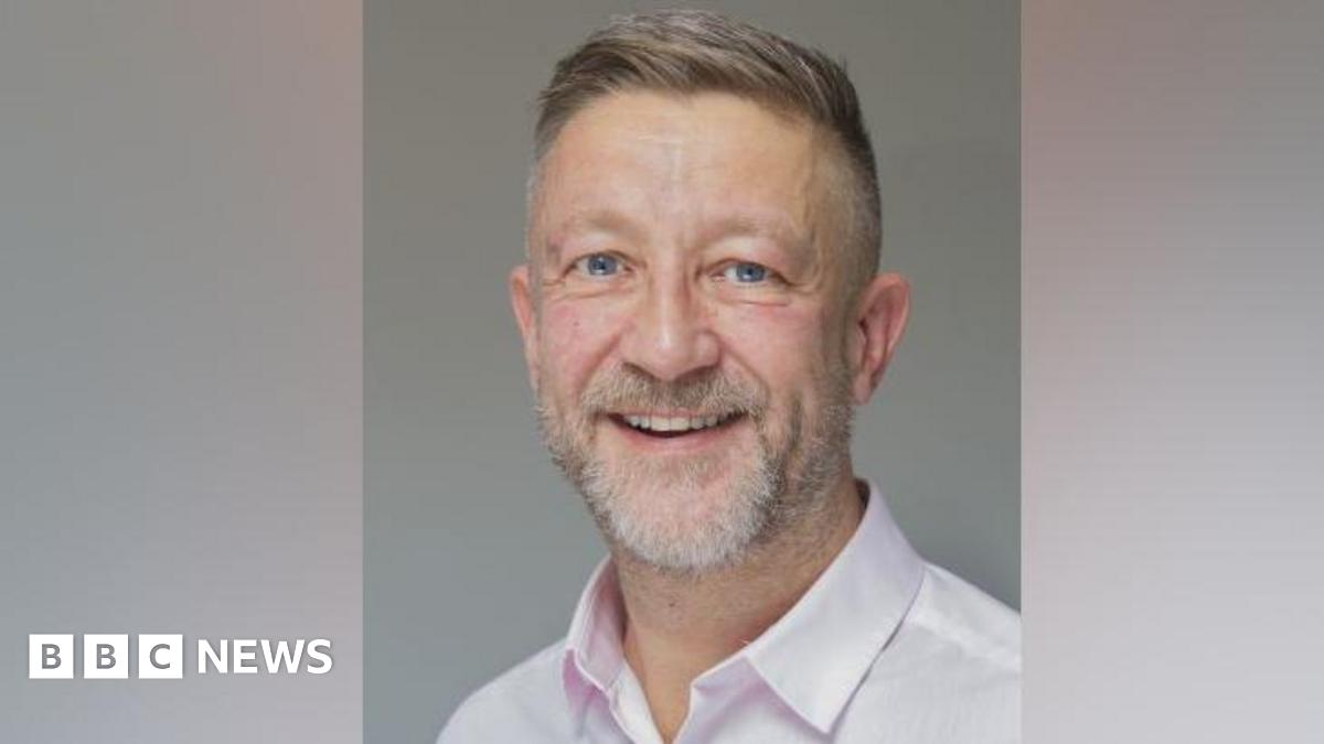 Young 18 year old man sits in the passenger seat of a black VW car, his arm resting on the open window as he looks to camera