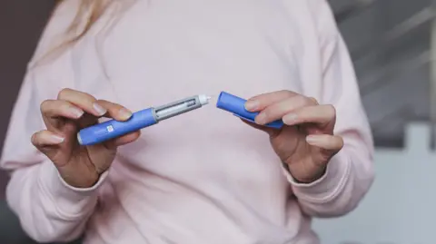 Getty Images Person preparing a weight-loss injection. They have taken the lid off the blue pen to expose the needle.

