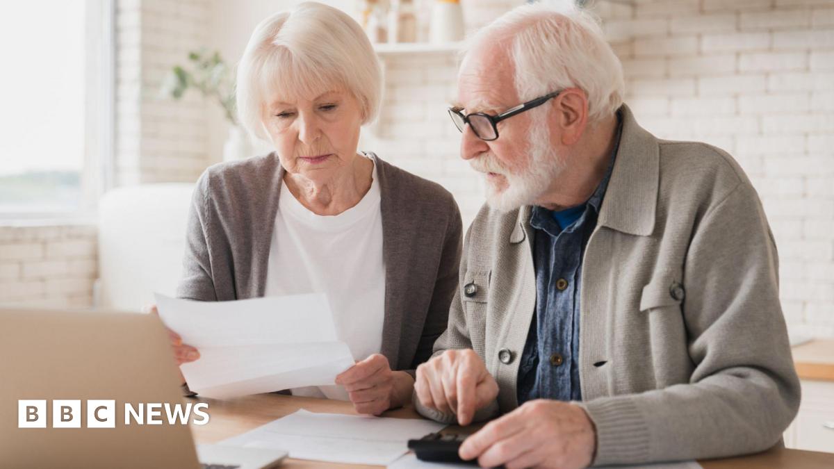 Older man and woman sit at a table in a kitchen with paperwork and a laptop in front of them