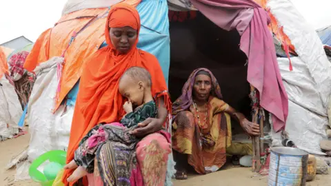 Reuters Buney Aayow Ibrahim, a Somali woman affected by the worsening drought due to failed rainy seasons, holds her three-year-old child Sadia Salas Abdi as her grandmother Habiba Osman looks on, next to their makeshift shelter at the Alla Futo camp for internally displaced people, outside the Somalian capital Mogadishu on 23 September 2022.
