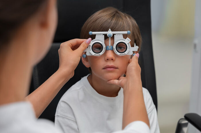Child undergoing an eye exam with an optometrist using a phoropter, illustrating Dr. Google versus real doctor debates.