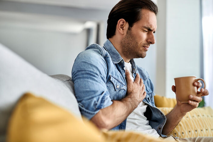 Man clutching chest in pain holding a mug, illustrating times Dr Google argued with a real doctor about health issues.
