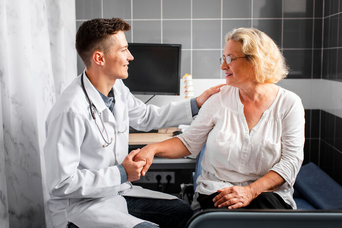 Young male doctor reassuring senior woman in a clinic setting, illustrating real doctor patient care and trust.