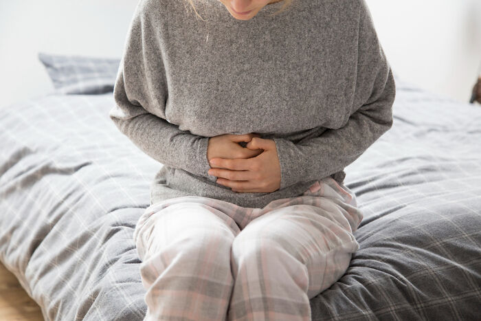 Person in pajamas sitting on bed, clutching stomach, illustrating the concept of Dr. Google versus real doctor advice.