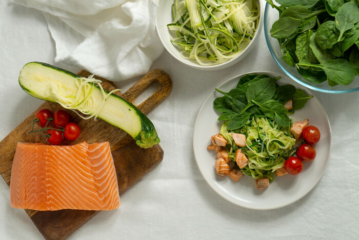Fresh salmon, spiralized zucchini, cherry tomatoes, and spinach prepared on a white table, related to Dr Google and real doctor debates.