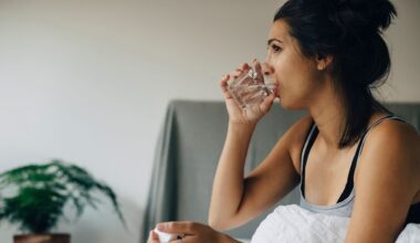 A woman sits in bed drinking a glass of water.