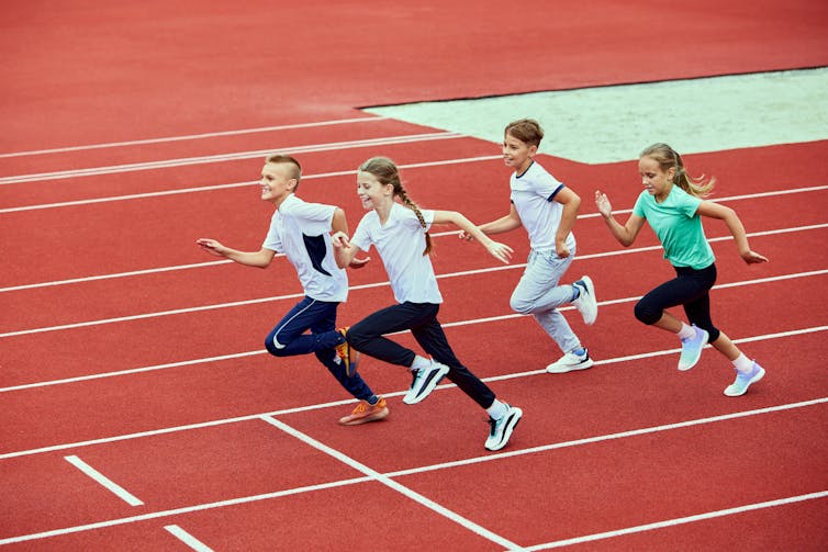 Four children running on an outdoor track.