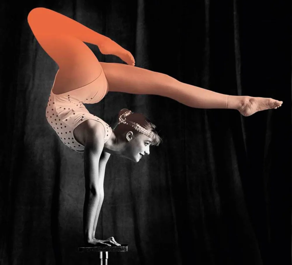 Side on photo of a gymnast performing a hand stand with their legs bent over their head