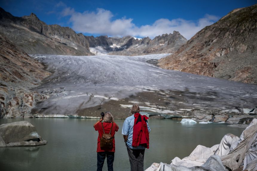 Two tourists face the melting Rhone Glacier on September 12, 2025. Switzerland's glaciers are disproportionately impacted by climate change and have shed a quarter of their mass in the past decade alone.
