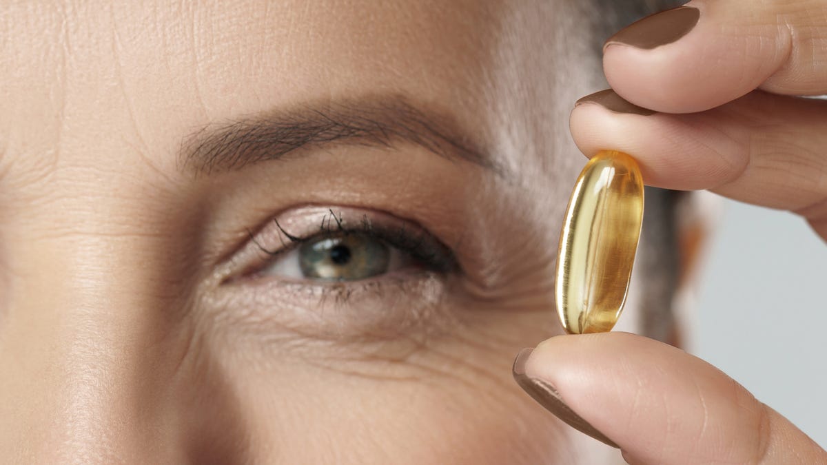 A person holding a vitamin near their blue-green eye.