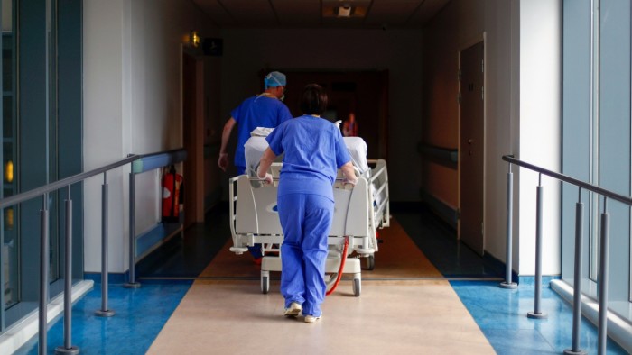 Medical staff in blue scrubs push a patient on a hospital bed down a corridor at The Royal Blackburn Teaching Hospital.