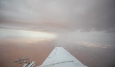 A view from a plane wing shows rain falling from dark clouds over a desert landscape during a cloud-seeding mission.