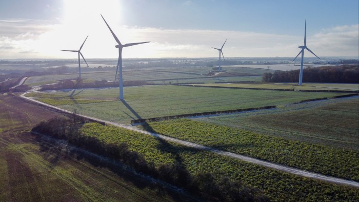 Several large wind turbines stand in open fields at an onshore wind farm under a clear sky.