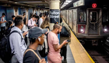 Commuters wait on the platform at Fulton Street subway station as a 5 train arrives during morning rush hour.