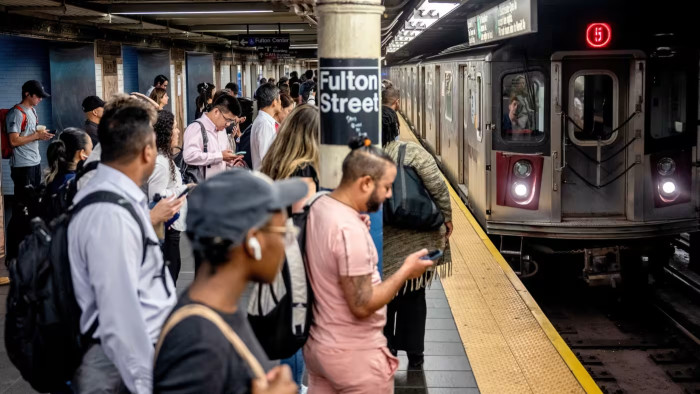 Commuters wait on the platform at Fulton Street subway station as a 5 train arrives during morning rush hour.