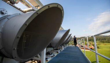 Several large circular Direct Air Capture fans on a rooftop with a person walking along the platform, overlooking a rural landscape.