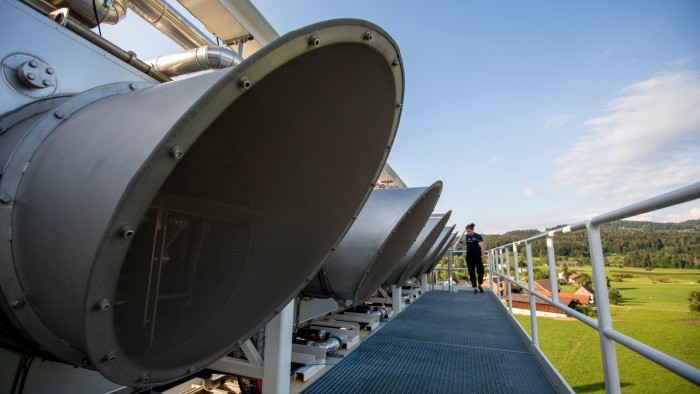 Several large circular Direct Air Capture fans on a rooftop with a person walking along the platform, overlooking a rural landscape.