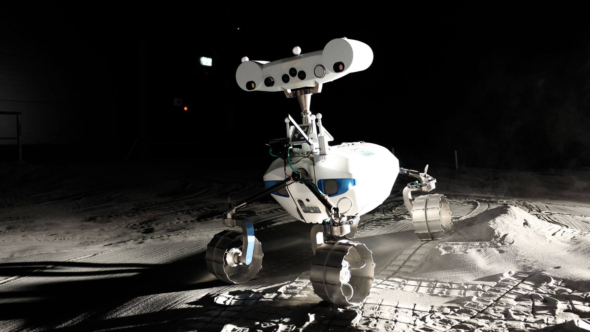 Two white rovers lean over simulated gray lunar dust.