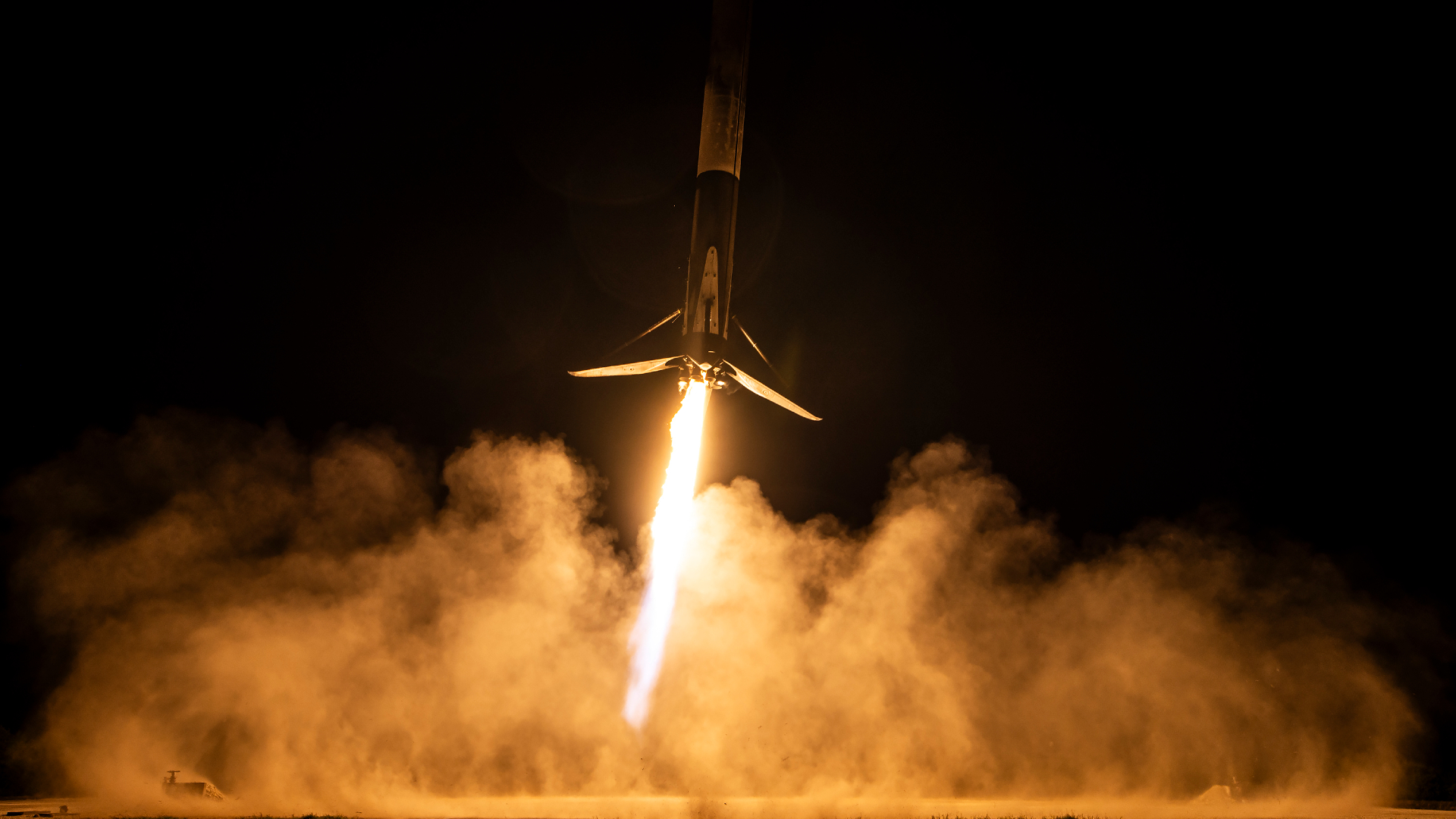 A rocket blazes up into a night time sky with glowing orange clouds of smoke illuminated by the tail of the rocket in the night