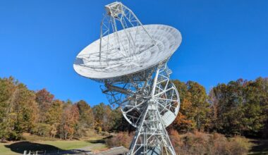 a large white, round antenna surrounded by trees with fall foliage