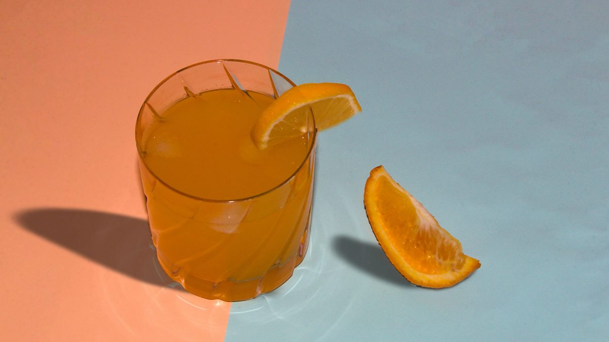 A glass of juice in a tumbler with two orange slices one next to the glass and one on the rim
