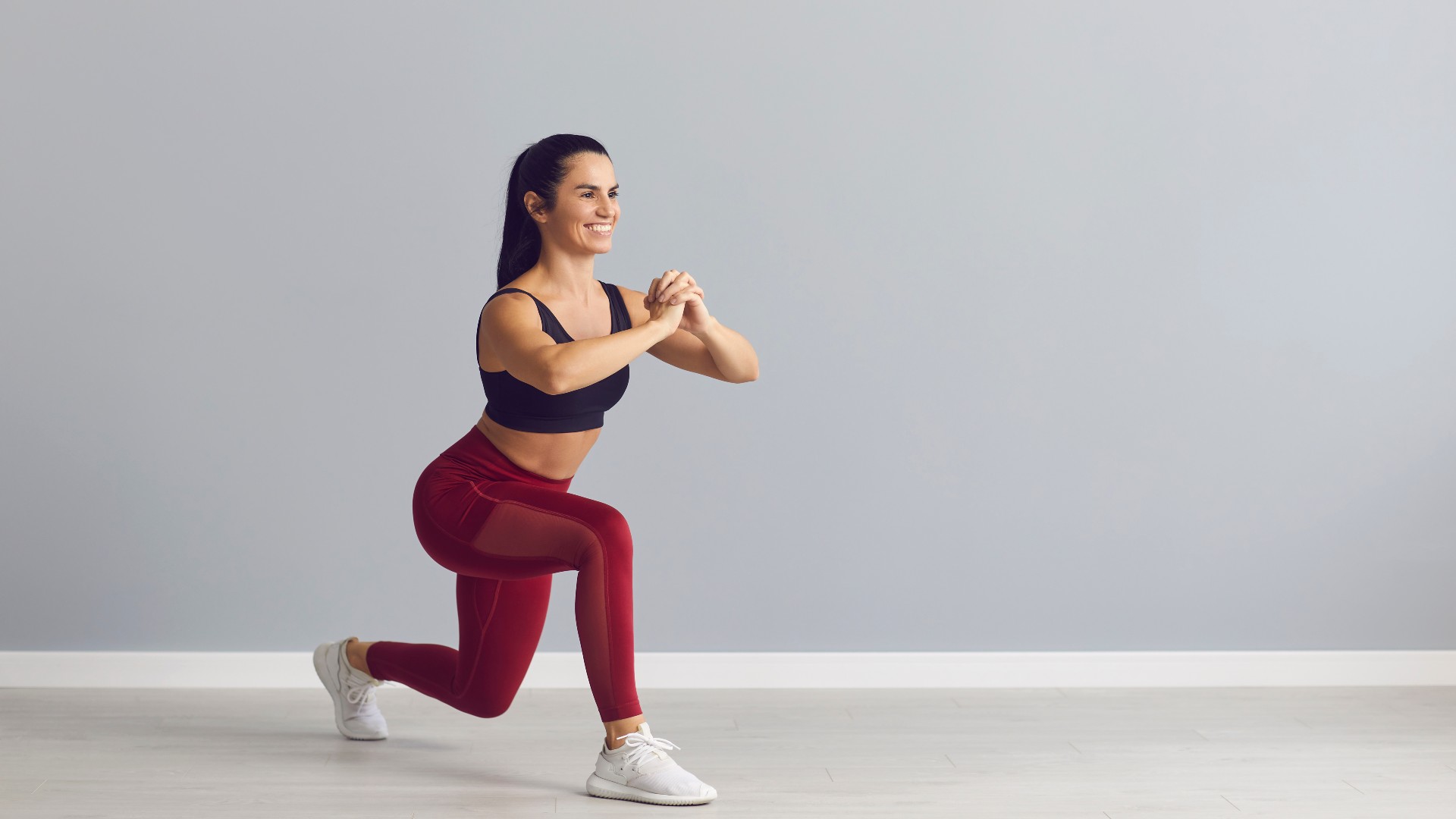Woman performing a curtsy lunge during glute workout against grey studio backdrop