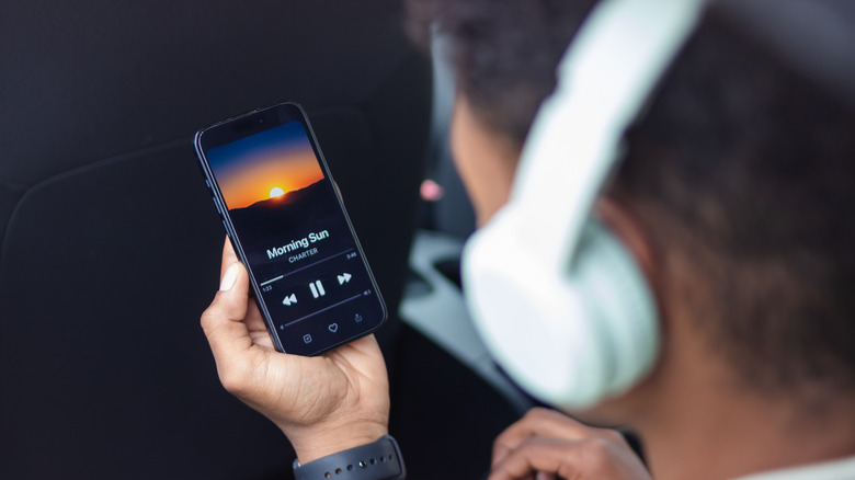 Person with headphones on holding a phone with a media player on the screen.