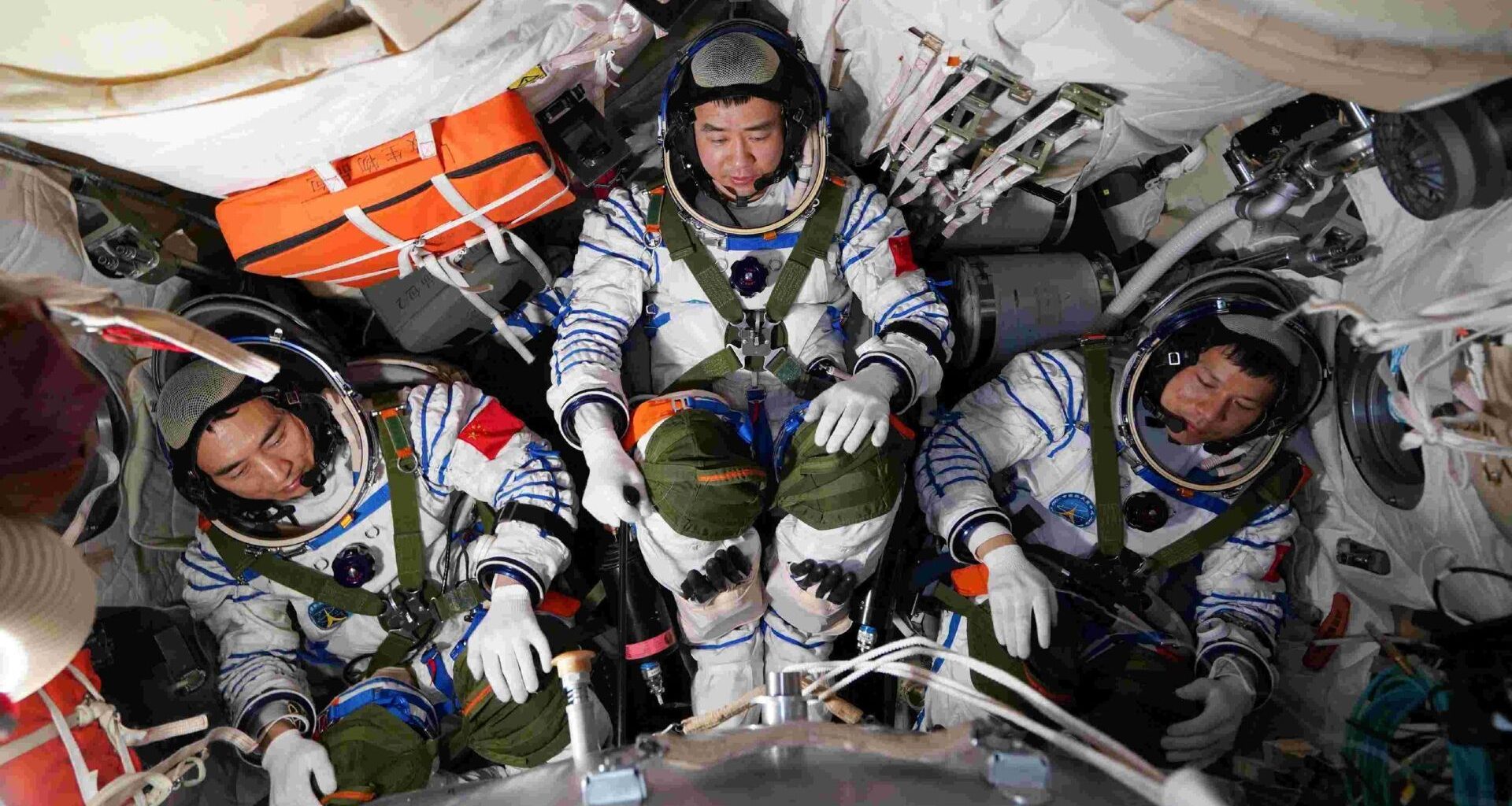 A photograph of three astronauts wearing white space suits huddled in a spacecraft.